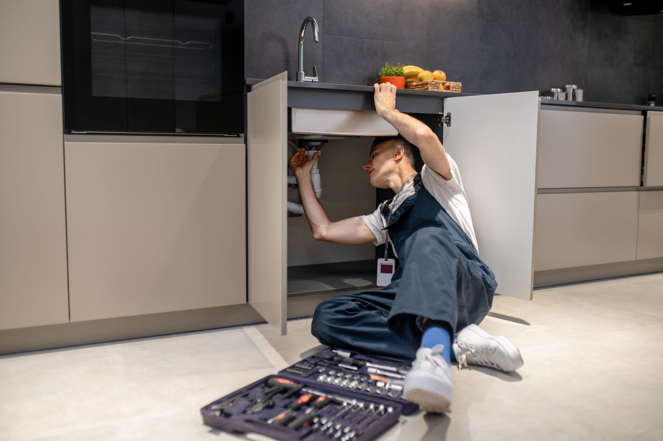 Kitchen Plumbing Services man reclining inspecting pipe under kitchen sink